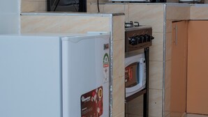 A compact kitchen with a refrigerator, microwave, stove, and coffee maker. - Couple Friendly Studio Apartment In Pangani (Nairobi)