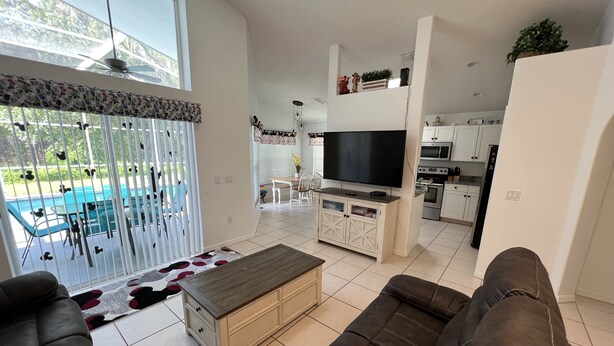 En moderne stue med sofa, fjernsyn og spiseplads med udsigt til poolen.