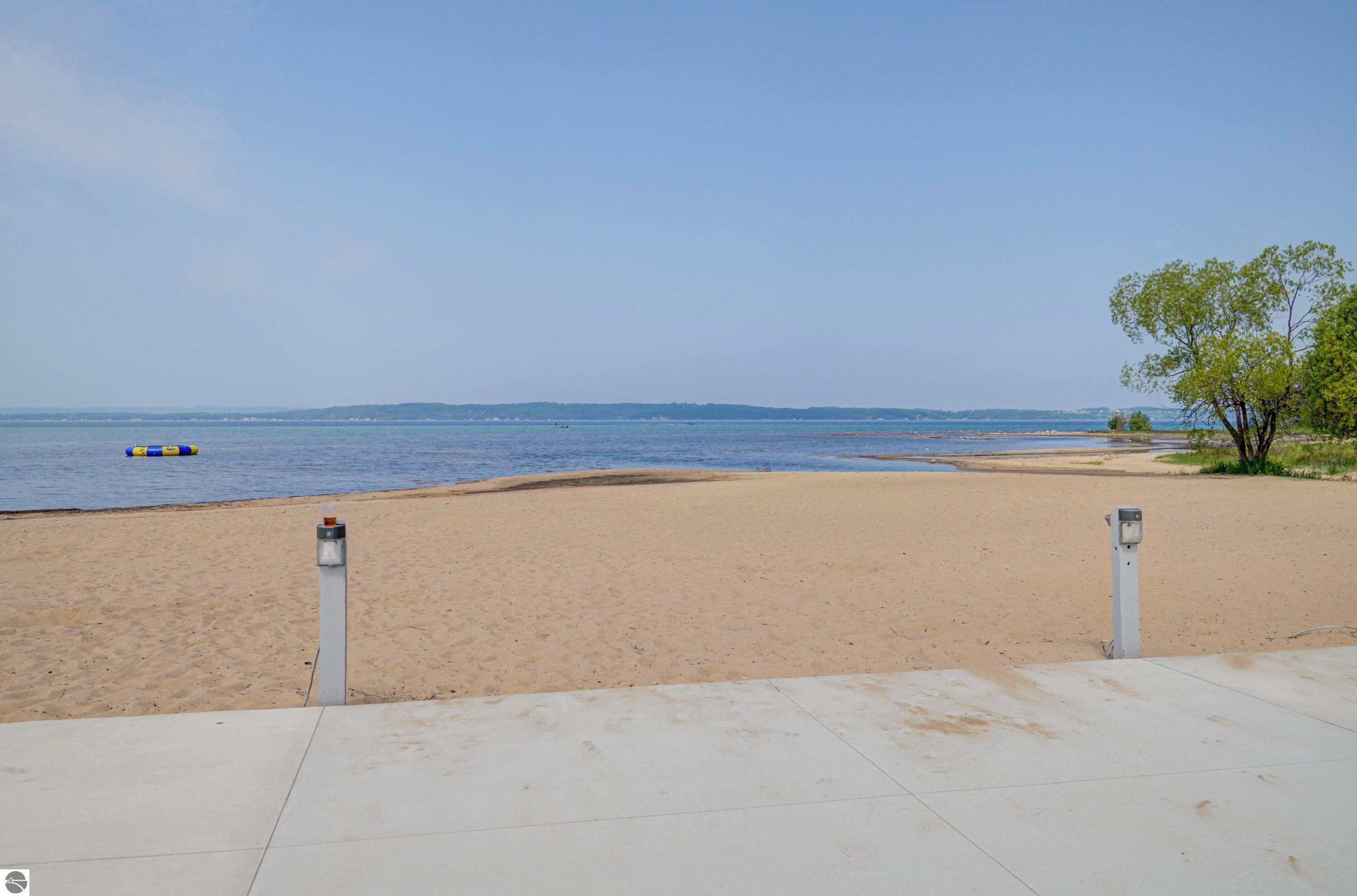 Ein Strand mit sandigem Ufer, blauem Himmel und einer entfernten Landansicht über dem Wasser.