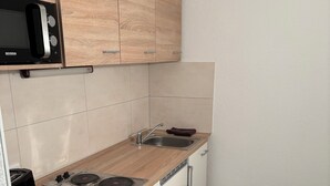 A compact kitchen with wooden cabinets, a microwave, a sink, and a built-in stove. - Cozy vacation apartment opposite Ammelshain Castle (Ammelshain)