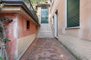Un carrer estret amb una porta verda, una escala i un edifici amb una paret rugosa.