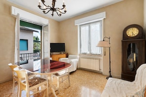 Une pièce avec une table en verre, des chaises, un téléviseur, une horloge et un radiateur.