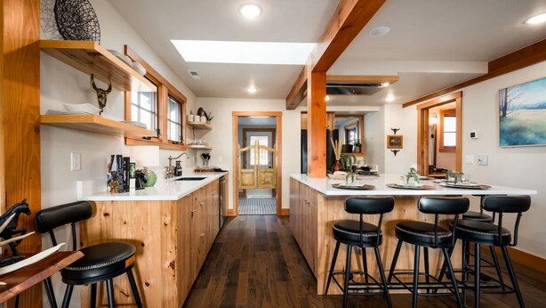 Una cocina con armarios de madera, una isla central con taburetes de bar y vistas al área de comedor.