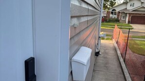 Fachada residencial con una puerta blanca, un buzón y una acera que conduce a una calle con una cerca roja.