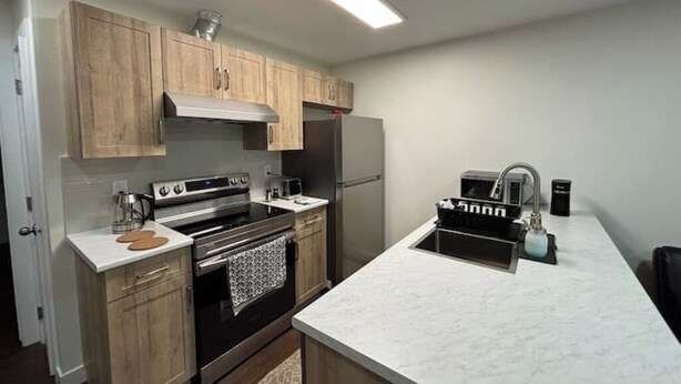 Cocina moderna con armarios de madera, estufa de acero inoxidable, horno empotrado, refrigerador y pileta con grifo.