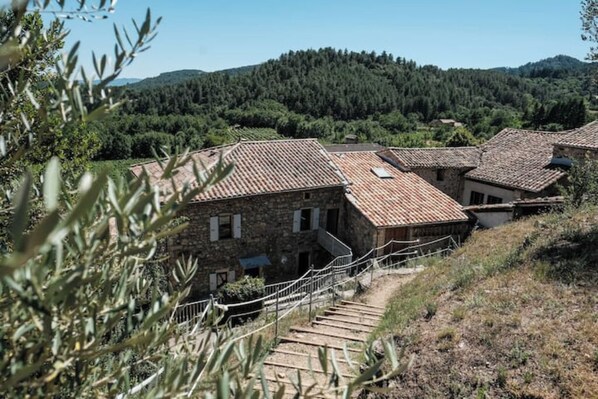 A stone building with a tiled roof, surrounded by olive trees and hills. - Le mas de Jeanne (Rocher)