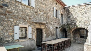 A stone building with a courtyard, a wooden table with chairs, and a small table. - Le mas de Jeanne (Rocher)