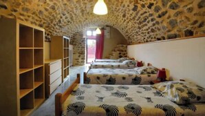 A room with stone walls and a sloped ceiling, featuring two beds with patterned bedding and a wooden bookshelf. - Le mas de Jeanne (Rocher)