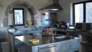 A modern kitchen with a central island, stainless steel appliances, and a window providing natural light. - Le mas de Jeanne (Rocher)