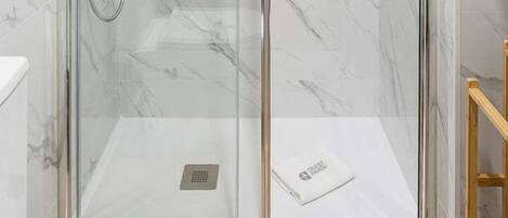 A glass-enclosed shower with a handheld showerhead and a wall-mounted faucet.