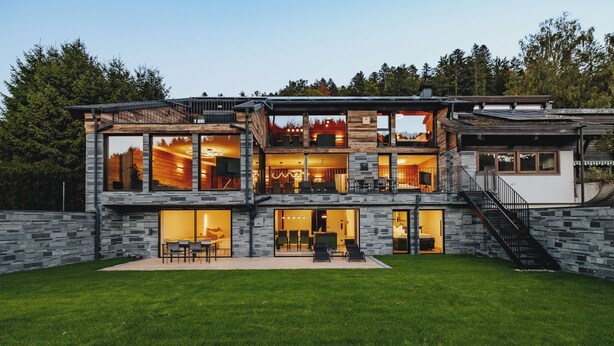 A modern two-story house with large windows, a stone facade, and a well-maintained lawn.