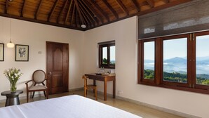 Une chambre à coucher comprenant un lit, un bureau, une chaise, une fenêtre donnant sur les montagnes et une porte.