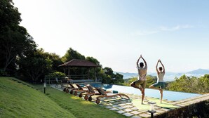 Un espace piscine agrémenté de chaises longues et d’un kiosque, entouré de verdure et avec des montagnes en toile de fond.