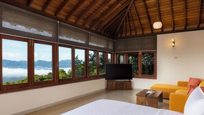 Une chambre spacieuse dotée de grandes fenêtres, d’un téléviseur à écran plat, d’un lit, d’un canapé et d’une table basse en bois.