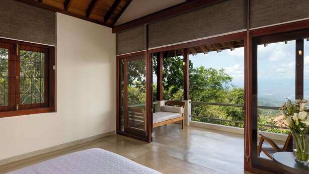 Une chambre à coucher avec un lit, un banc en bois et un balcon donnant sur un paysage verdoyant.