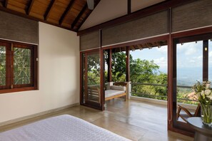 Un dormitorio con cama, un banco de madera y un balcón con vistas a follaje.