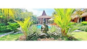 Un jardin paisible agrémenté d’une statue, d’un bâtiment de style traditionnel et d’une piscine.