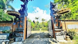 Un portail traditionnel orné de sculptures complexes, qui mène à un sentier bordé d’une végétation luxuriante et s’ouvre sur un ciel bleu azur.