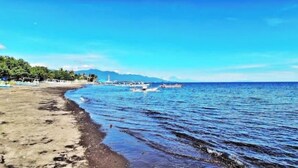 A beach with boats, clear skies, and distant mountains. - KAMAR HIJAU. Comfortable 1BR Beachfront Apartment With AC, Pool & Kitchenette. (Tegallengah)