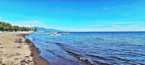 A beach with boats, clear skies, and distant mountains. - KAMAR HIJAU. Comfortable 1BR Beachfront Apartment With AC, Pool & Kitchenette. (Tegallengah)