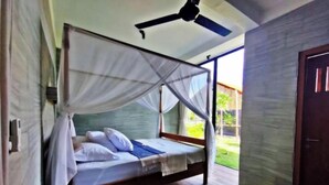 A single bed with a canopy, wooden flooring, a ceiling fan, and a view of the outdoors. - KAMAR HIJAU. Comfortable 1BR Beachfront Apartment With AC, Pool & Kitchenette. (Tegallengah)