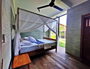 A single bed with a canopy, wooden flooring, a ceiling fan, and a view of the outdoors. - KAMAR HIJAU. Comfortable 1BR Beachfront Apartment With AC, Pool & Kitchenette. (Tegallengah)