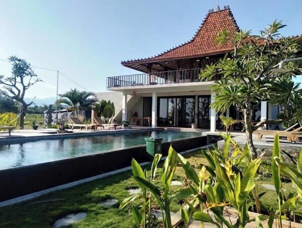 Una casa moderna con una gran piscina, un porche cubierto y abundante vegetación.