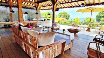 Eine Holzterrasse mit einer Sitzecke, einem Tisch und Blick auf das Meer.