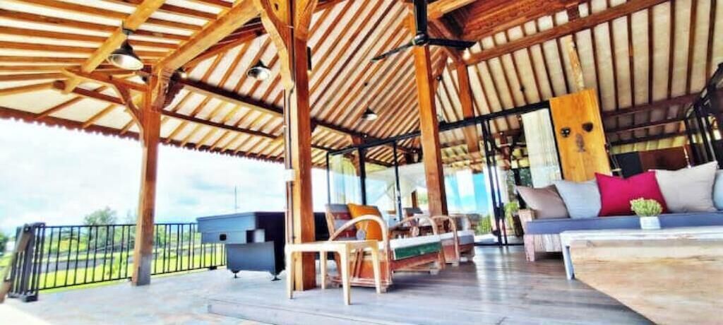 Une terrasse extérieure couverte, avec des poutres en bois, un canapé avec des coussins et une table à manger.