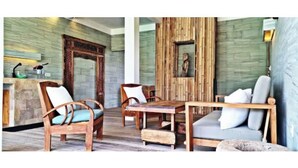 A room with a wooden dining table, two wooden chairs, a sofa, and a wooden cabinet. - KAMAR MERAH. Comfortable 1BR Beachfront Apartment With AC, Pool & Kitchenette. (Tegallengah)