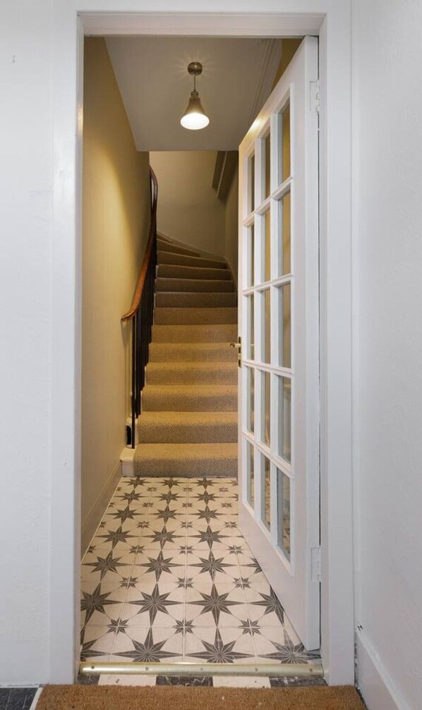 A hallway with a carpeted staircase leading to a door with glass panels.