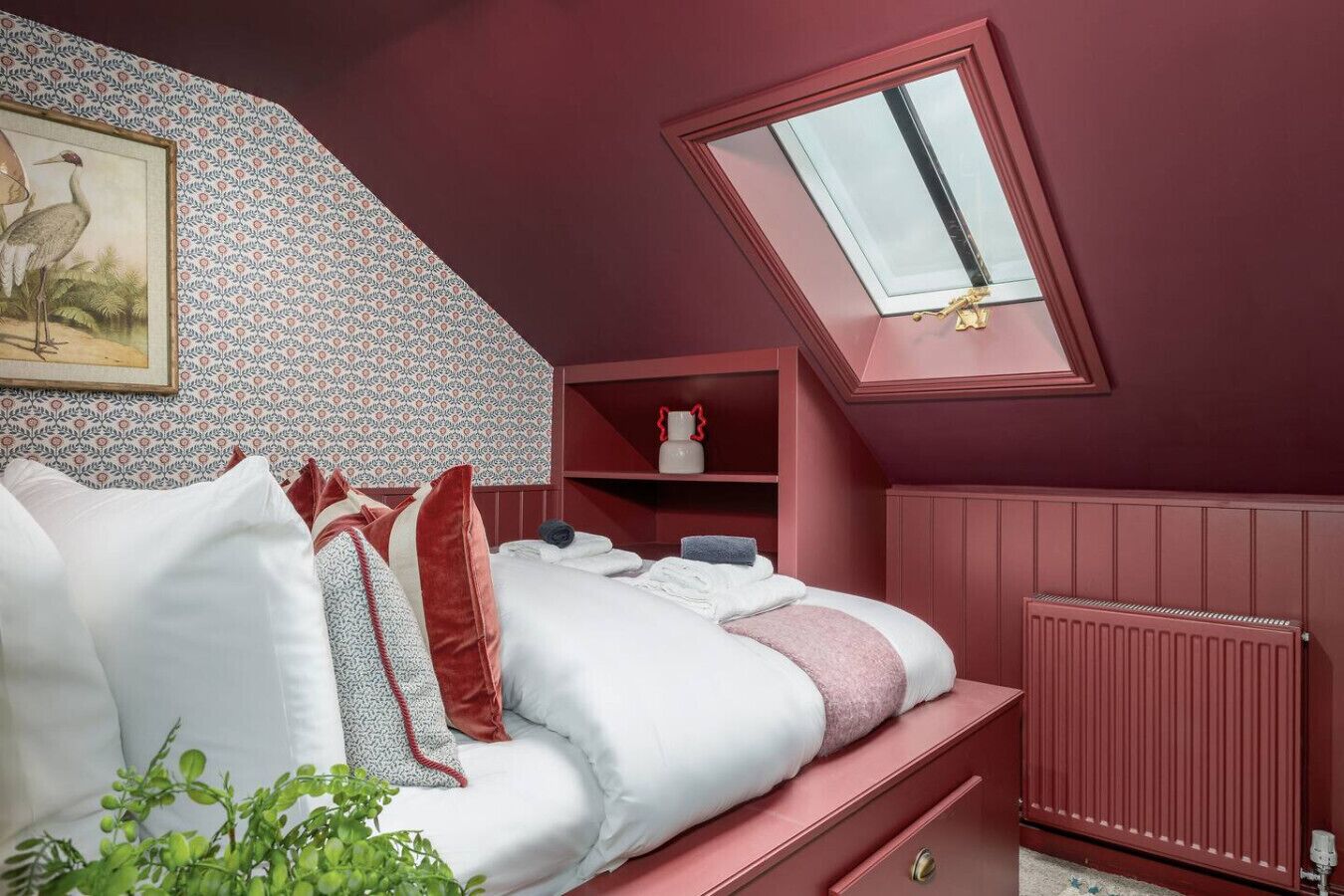 Quarto com teto inclinado, claraboia, radiador e cama com almofadas e cobertor.