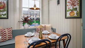 Comedor con mesa de madera dispuesta para cuatro, lámpara colgante y ventana con vista a un invernadero.