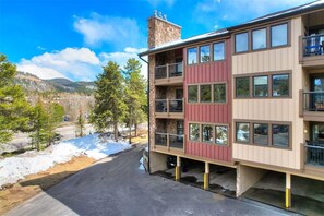 A multi-story building with balconies, a stone chimney, and a parking area with snow. - Corner Unit in the Center of Town, Walk to Lifts (Breckenridge)