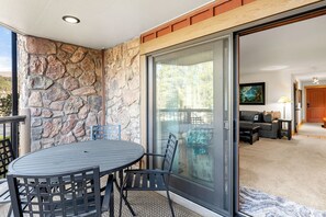 A patio with a stone wall, a sliding glass door leading to a living room, and a round table with chairs. - Corner Unit in the Center of Town, Walk to Lifts (Breckenridge)