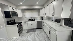 A modern kitchen with white cabinetry, a built-in microwave, a coffee maker, and a black countertop. - Luxury House Perfect location-3BR Sterling Heights  (Sterling Heights)
