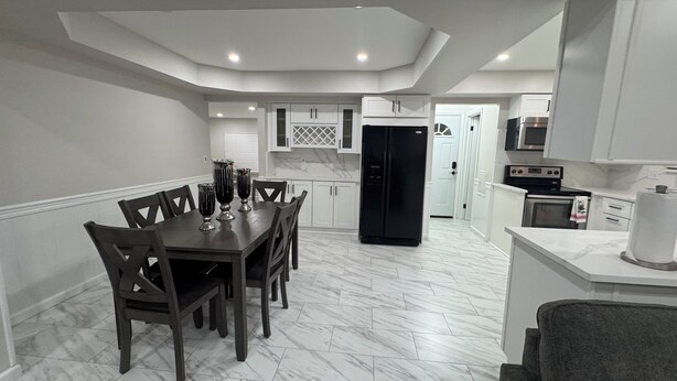 A modern kitchen with white cabinetry, a black refrigerator, and a dining area with a marble floor. - Luxury House Perfect location-3BR Sterling Heights  (Sterling Heights)