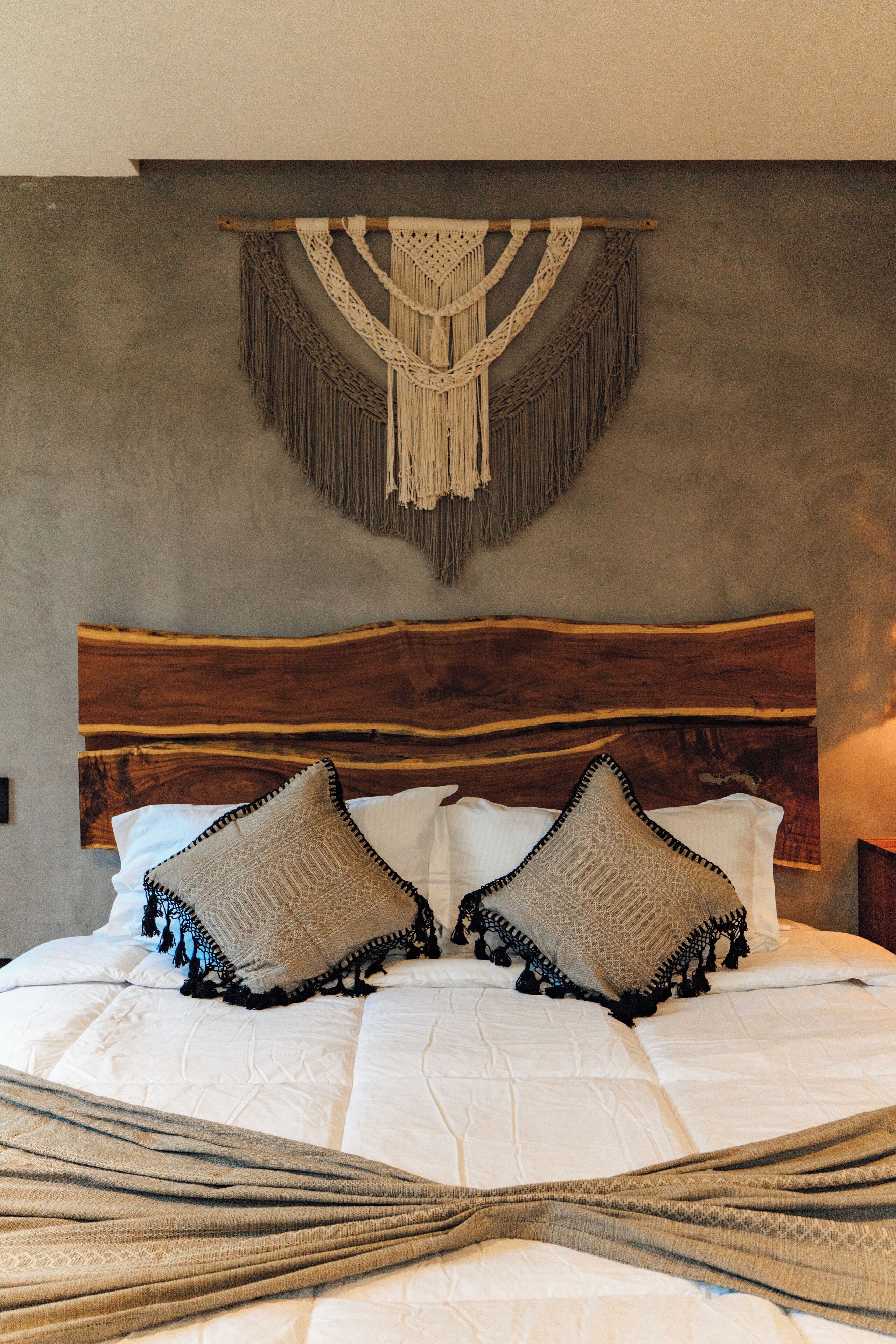 A bed with a wooden headboard, two decorative pillows, and a macrame wall hanging.