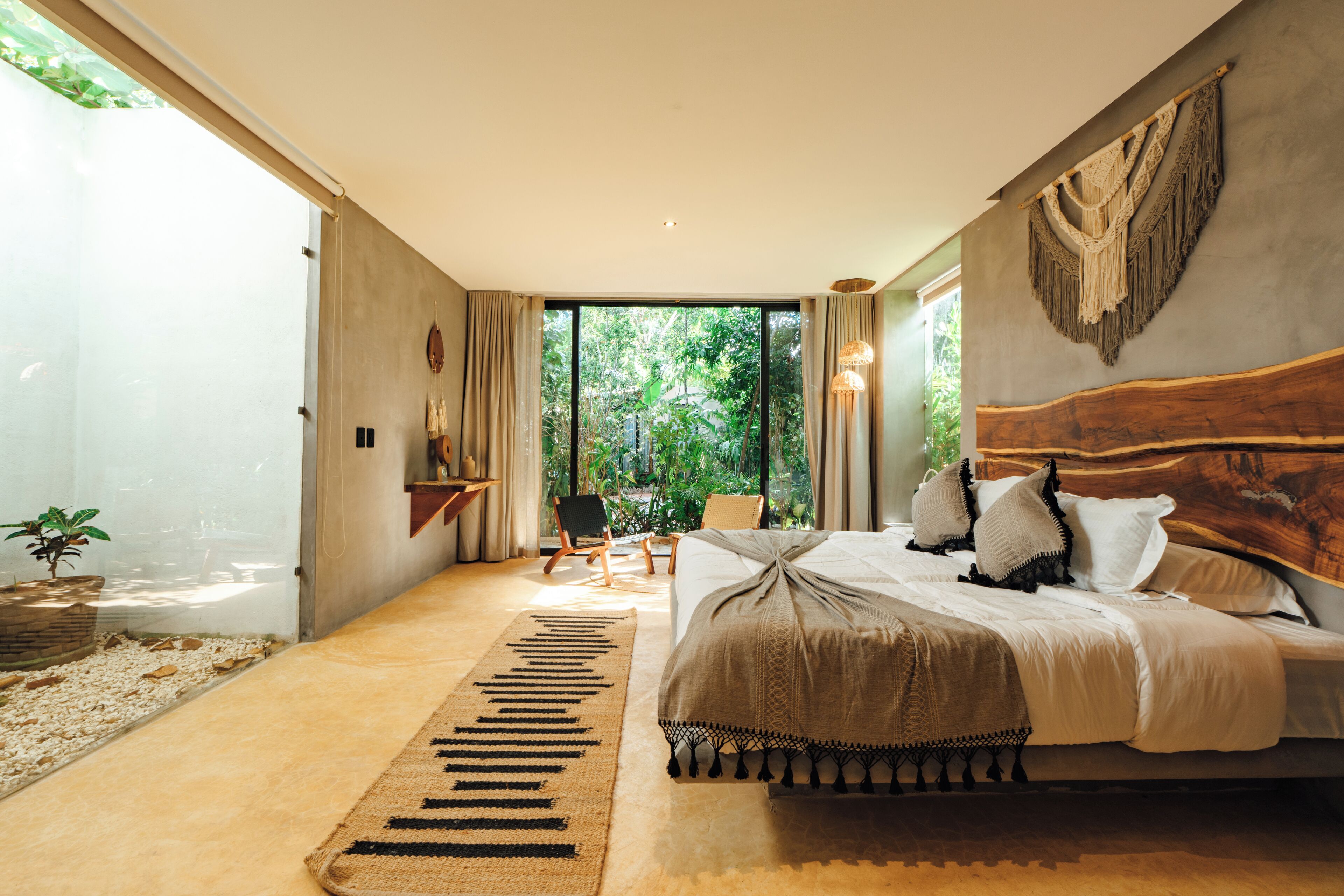Een moderne slaapkamer met een groot bed, uitzicht op groen buiten het raam, en een klein zithoekje.