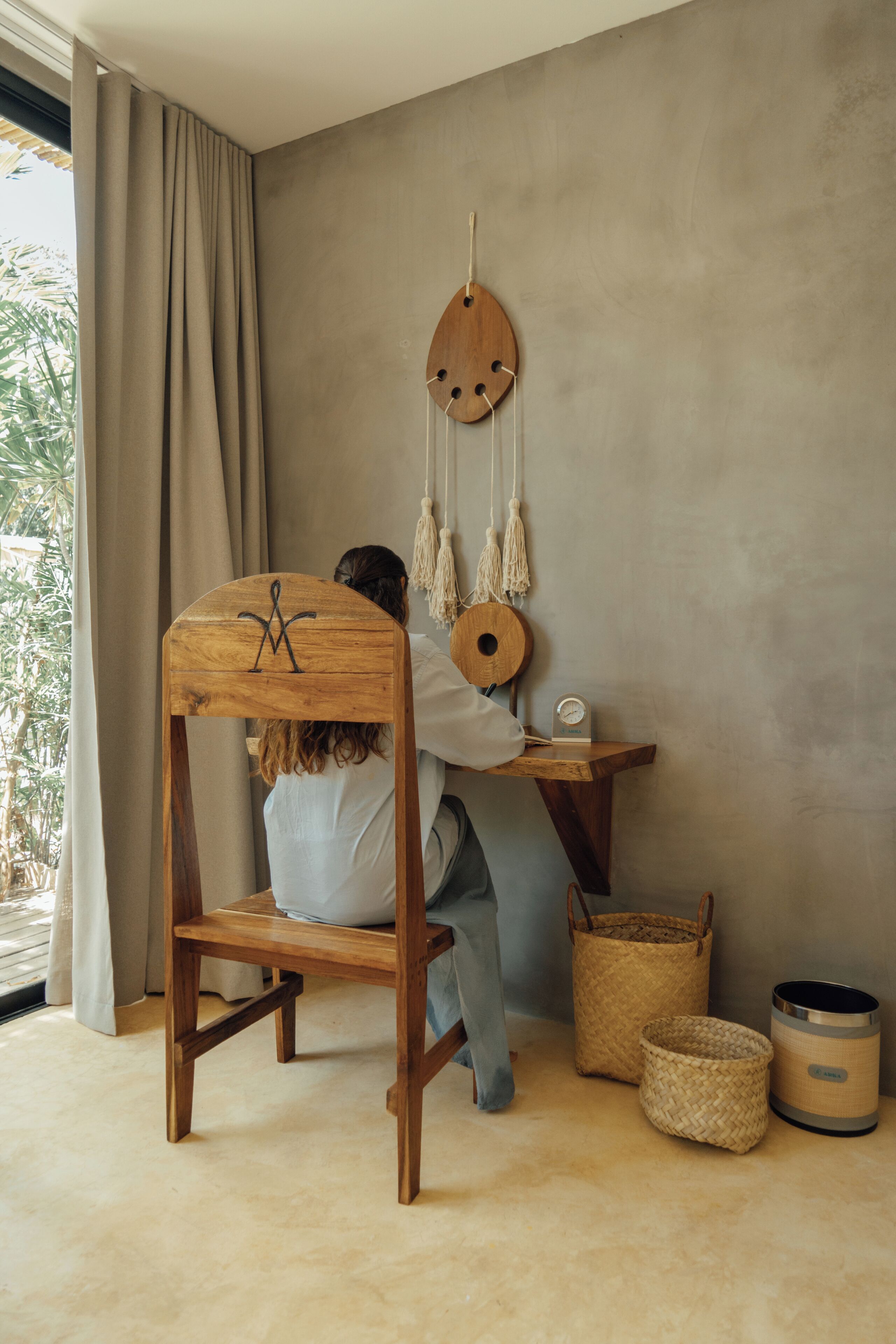 A room with a wooden chair, a desk, and a hanging macrame decoration.