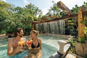 A couple in a pool with a waterfall backdrop, holding drinks. - ARKA TULUM (Tulum)