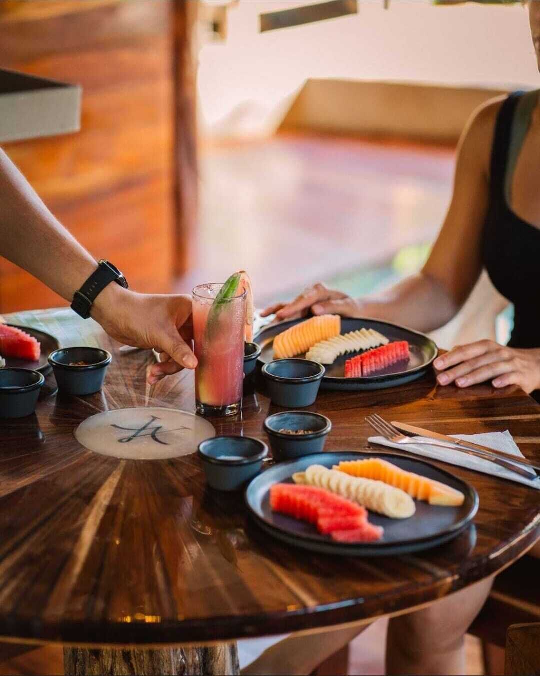 A wooden table with plates of sliced fruits, a glass of drink, and small bowls, likely in a restaurant setting.