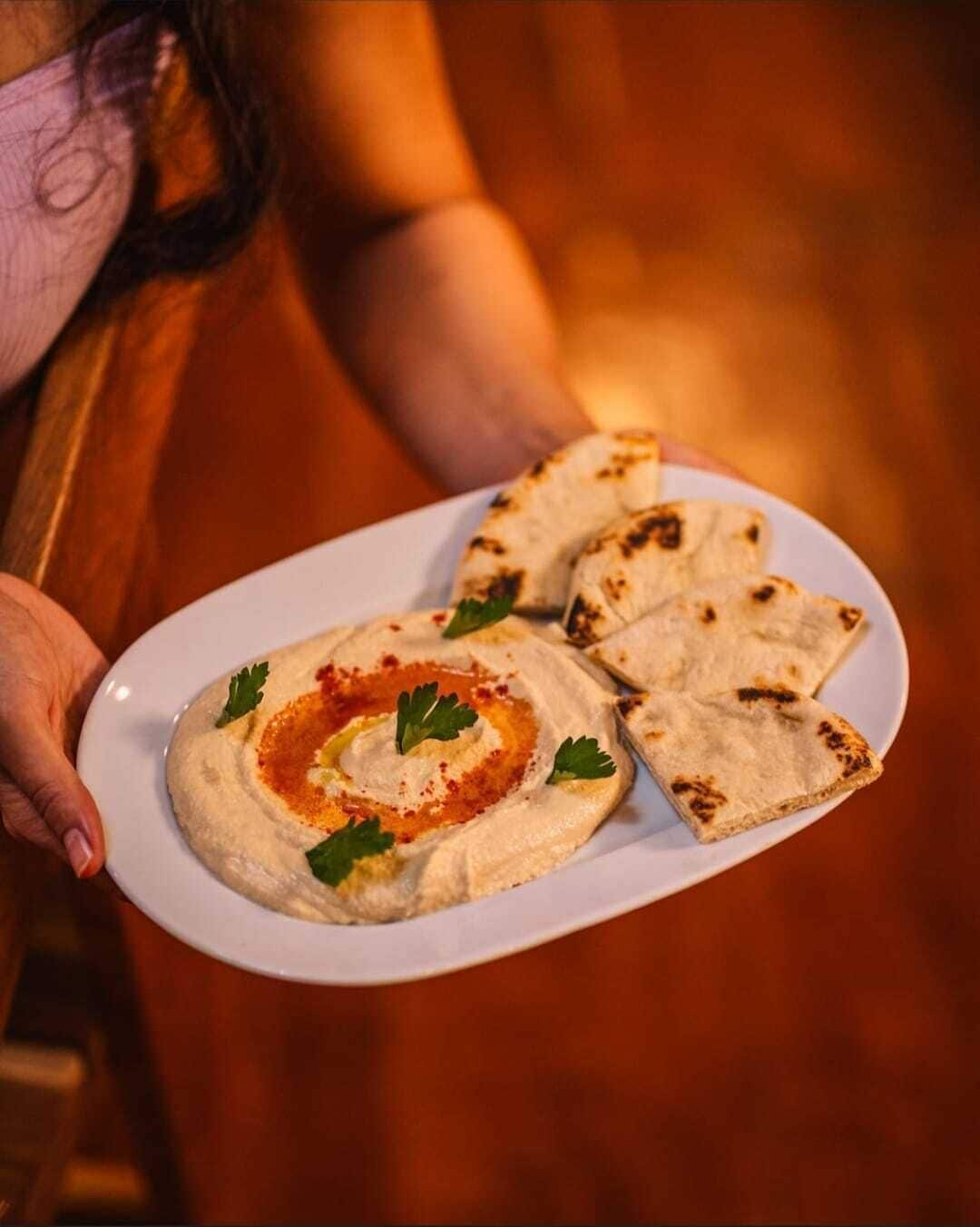 A person holding a plate with hummus and pita bread.