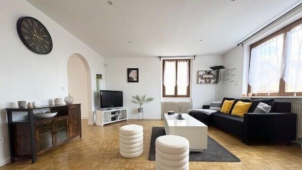 A modern living room with a wooden floor, a black sofa with yellow cushions, a white coffee table, and a television on a white stand. - The Dutt's cocoon: spacious and charming T3 (Duttlenheim)