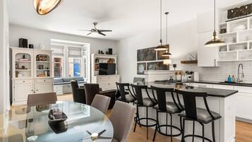 A modern kitchen with white cabinetry, a central island, and a dining area with a glass table and chairs.
