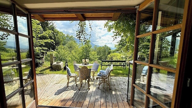 Terraza abierta con mesa y sillas, rodeada de vegetación y vistas a la montaña.