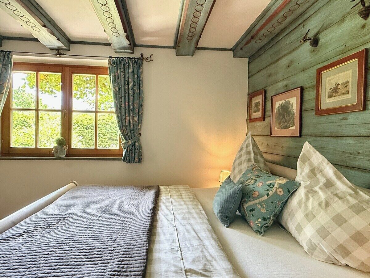 A bedroom with a bed, a window with curtains, and framed pictures on the wall.