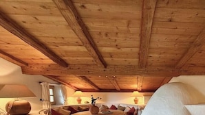 Una habitación con vigas de madera en el techo, un sofá, una lámpara y una ventana con cortinas.