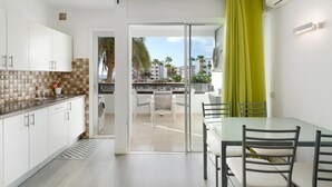 Una cocina moderna con armarios blancos, una mesa de comedor de cristal y vistas a un balcón con palmeras.