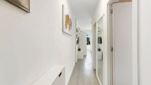 Un pasillo con paredes blancas, suelo de madera clara, una obra de arte enmarcada y una puerta al final.